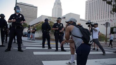 A demonstrator kneels in front of a row of police officers as protesters gather in downtown Los Angeles on May 27, 2020. AFP