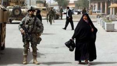 A woman walks past a US soldier patrolling in Baghdad. US combat troops are to pull out of Iraqi cities in June.