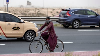 A cyclist covers his face as wind blows up sand in Dubai. Chris Whiteoak / The National