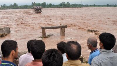 Indian villagers look on at a missing section of a bridge across the overflowing Tawi river that was swept away as flooding continues in the Mandal area of Jammu on September 6, 2014. AFP Photo