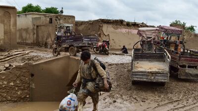 An Afghan man carries his belongings as he walks through a mud covered street following a flash flood after a heavy rainfall in Laqiha village of Baghlan-i-Markazi district in Baghlan province on May 11, 2024. At least 62 people, mainly women and children, were killed on May 10 in flash flooding that ripped through Afghanistan's Baghlan province, in the north of the country, a local official told AFP. (Photo by AFP)