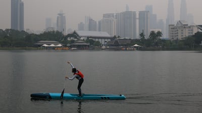 A woman paddleboards against the Kuala Lumpur skyline, blanketed in haze, as unhealthy air quality is reported in the city. EPA