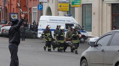 A police officer stops a car as Emergency Minisrty officers and firefighters carry a body to an ambulance car in downtown Moscow.