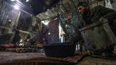 A Palestinian man removes a basin filled with water from a leaking roof inside his family tent made of tin and nylon sheets, as children huddle in a corner to watch television, on a rainy day in al-Amal (hope in Arabic) neighbourhood of Beit Lahia in the northern Gaza Strip. AFP