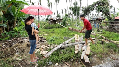 Aiza Tonida, carrying her two-year-old son, watches husband Jericho Caga picking up pieces of coco lumber. (Joey Reyna for The National / April 9, 2014)