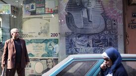 A woman talking on her mobile phone as she passes a currency exchange store in Cairo. Imported phone users face paying a hefty import tax. Bloomberg