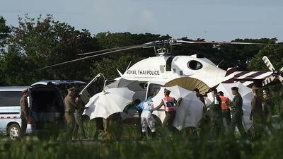 Police and military personnel use umbrellas to cover a stretcher near a helicopter and an ambulance at a military airport in Chiang Rai. AFP