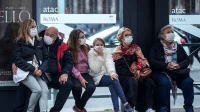 People wait at a bus stop, in Rome, Monday, March 9, 2020. AP