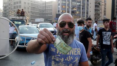 A man gestures with a currency note as Lebanese protesters block the roads with garbage bins and burning tires during protests after Saad Hariri abandoned efforts to form a new government, in Beirut, Lebanon, July 15. EPA