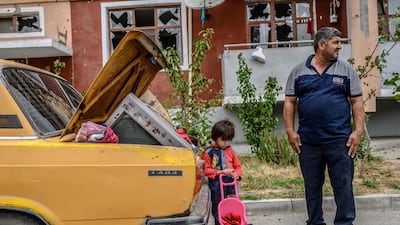 A man stands with his kid by a car outside a damaged apartment building after the family took their last belongings from their flat during a ceasefire during a military conflict between Armenia and Azerbaijan over the breakaway region of Nagorno-Karabakh. AFP