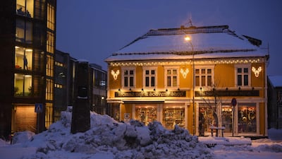 People walk near a tourist shop as it snows in downtown Tromso on January 11, 2019. At this time of year, daylight lasts about 2 hours, between 11am and 1pm. AFP