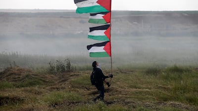 A demonstrator holds up Palestinian flags during clashes with Israeli troops along Israel's border with Gaza on March 30, 2018. Mohammed Salem / Reuters