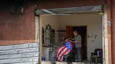 A boy draped in a cape in the colours of the US flag gets his hair cut at a damaged barbershop in Zawtar Al Gharbiy. AFP