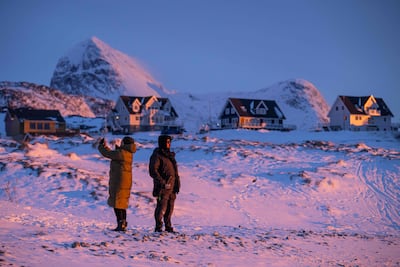 Locals stand on a snowy shoreline at dusk in Nuuk, Greenland. AFP