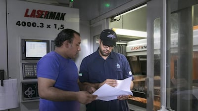 Ahmed Al Mazroei, left, works with Hassan Mohamed, programme operator of a laser-cutting machine at the 1,500-square-metre factory in Mussaffah. Silvia Razgova / The National