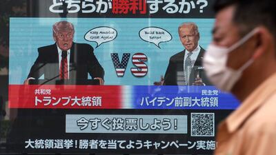 A man wearing a protective mask to help curb the spread of the coronavirus walks past a screen showing illustrations depicting Republican President Donald Trump, left, and Democratic candidate and former Vice President Joe Biden for an online voting to predict the winner in the Nov. 3 U.S. presidential election, in Tokyo Monday, Oct. 26, 2020. The Japanese letters at top read: "Which one will win in the Nov. 3 U.S. presidential election." (AP Photo/Eugene Hoshiko)