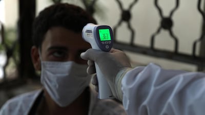 A medic checks the body temprature of a patient at a treatment centre in Ariha city, south Idlib, Syria, on August 25, 2020. EPA
