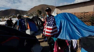 Daniel Castilla, 19, from Honduras, wears a US flag as he looks out over migrant tents at a former concert venue now serving as a shelter, in Tijuana, Mexico. AP Photo