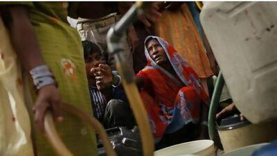 A New Delhi slum resident reaches to try to get the hose as she and others wait to fill containers at a water depot: two out of 50 of the city's drinking-water taps tested positive for a 'super superbug' gene.