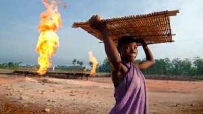 A woman carries tapioca seeds next to a gas flare fire in Nigeria.