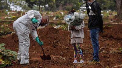 An employee digs next to relatives of a person who died from COVID-19 at the Vila Formosa cemetery, in the outskirts of Sao Paulo, Brazil on May 20, 2020. AFP