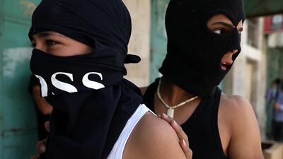 Palestinian youths wearing balaclavas take cover while hurling stones at an Israel Defense Force (IDF) checkpoint in the West Bank city of Hebron, 5 June, 2020. EPA