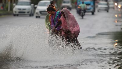 Indian women wade across a flooded road in Jammu.