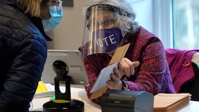 Poll worker Alice Machinist, of Newton, Mass., right, wears a mask and shield out of concern for the coronavirus while assisting a voter, left, with a ballot during early in-person general election voting, at the Newton Free Library, in Newton, Massachusetts. AP Photo
