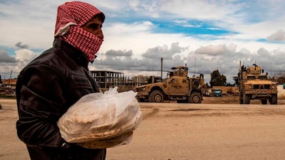 A man carrying bags of bread walks as a patrol of US military vehicles is seen in the town of Tal Tamr in the northeastern Syrian Hasakeh province along the border with Turkey. AFP