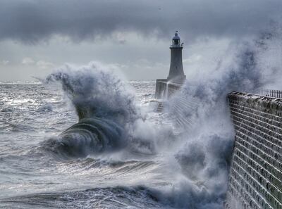 Waves crash over the pier at Tynemouth on England's north-east coast. PA