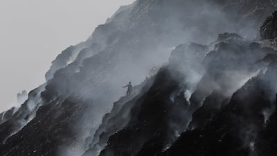 A waste collector climbs down while looking for recyclable materials as smoke billows from burning rubbish at the Bhalswa landfill site on World Environment Day in New Delhi, India. Reuters