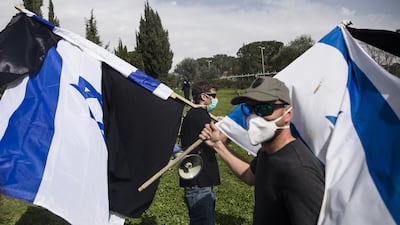 Demonstrators wearing protective mask hold the Israeli flag and a black flag as they protest outside the Israeli Parliament in Jerusalem, Israel. Getty