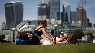 People relax in the sun of the bank the River Thames, with the The City of London financial district in the distance, in London, Britain, June 16, 2022. Reuters