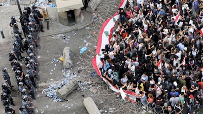 Demonstrators carry Lebanese flags as riot police stand guard behind barbed wire during an anti-government protest in Beirut on October 19, 2019. Reuters