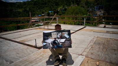 Luis Cosme poses on the roof of his new home as he holds a printed photo taken on October 1, 2017 showing him on his property destroyed by Hurricane Maria.