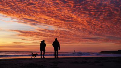 Dog walkers are silhouetted by a spectacular sunrise over Tynemouth beach, North Tyneside, on Monday. PA