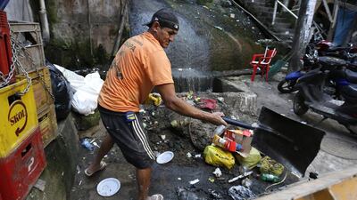 A man shovels garbage away from the base of a sewage waterfall running down stairs and next to walkways in Rocinha Favela. Barbara Walton / EPA