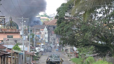 A Philippine marines armoured personnel carrier speeds away as black smoke billows from burning houses after military helicopters fired rockets at militant positions in Marawi on May 30, 2017. Ted Aljibe / AFP