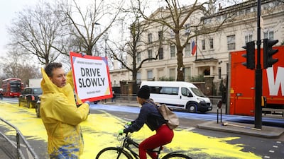 A member of Led by Donkeys holds a sign warning drivers to travel slowly over the paint