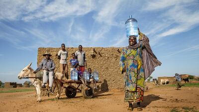 Fouré Moussa stands, balancing a large plastic container of water atop her head, while (background, left-right) her husband, Moumouni Alassane, and five children sit nearby with the family’s donkey, in the village of Bara Bangou in Niger. With them are four large plastic containers bearing a combined total of 80 litres of water, the amount the family uses daily for cooking and drinking. During the rainy season, they use ponds created by rainfall to wash dishes and clothes. Ms. Moussa fetches water from a borehole that is two kilometres away and serves over 400 families; to avoid long queues, she goes at night. It takes her 30 minutes to walk there, plus another 15 minutes for every container of water she needs to fill. Courtesy Unicef