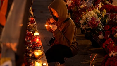 A young woman crosses herself as she lights a candle at an informal street memorial near the Kremlin, Moscow, for the Wagner Group members killed in the plane crash. AP