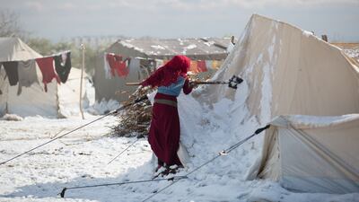 A Syrian woman scrapes snow from her destroyed tent after a snowstorm.