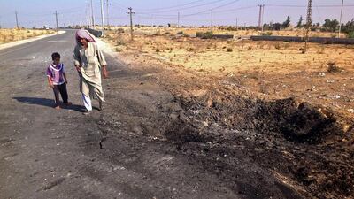 A man and child walk past a crater from a suicide bomb attack on the road between the border town of Rafah and the coastal city of El Arish. Ahmed Abu Deraa / AP