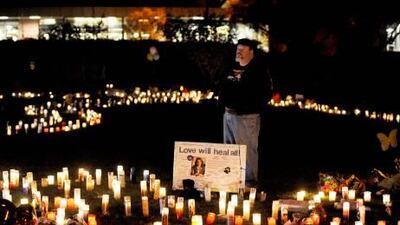 A man stands behind a poster with the portrait of the Representative, Gabrielle Giffords, that reads 'Love Will Heal All', in Arizona.