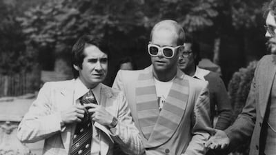 Elton John, in a jacket with a striped lapel and white sunglasses, with his manager John Reid on their way to a luncheon in honour of Buddy Holly in Holland Park, London on September 8, 1976. Getty Images