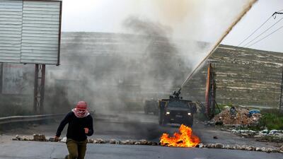 A Palestinian girl with his face covered with traditional chequered keffiyeh runs away from an Israeli water cannon. AFP