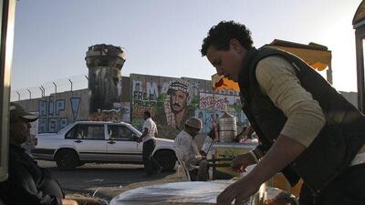 A Paestinian vendor sells sweets by a section of Israel's separation barrier, at the Kalandia checkpoint.