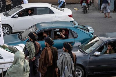 An Afghan woman (C) films Taliban security personnel celebrate the anniversary of the Taliban takeover, in front of the former US Embassy in Kabul, on August 14. AFP
