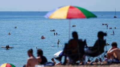 People gather on the beach while others cool off in the shallows during hot weather at Brighton, southern England. AP