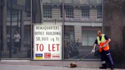 A street cleaner sweeps the pavement outside a building with a sign for office space "To Let" in its window, in central London.